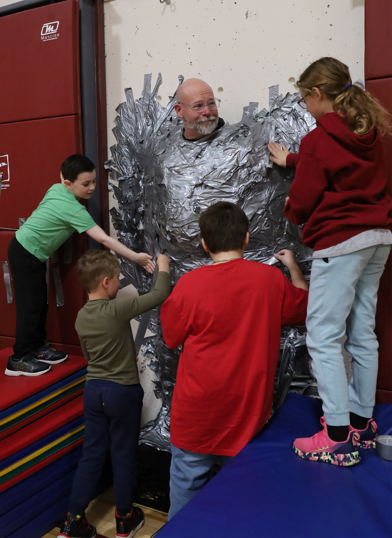 Harrington Elementary School students duct tape Principal Rob Asselin to the gymnasium wall on Thursday, April 30, as a fundraiser for the fourth grade class.